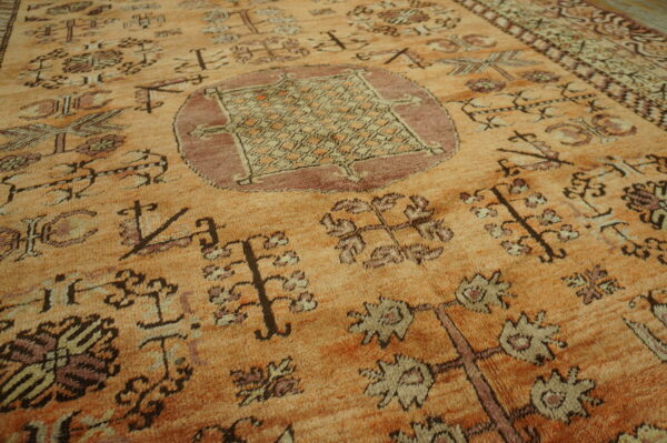 Textured orange rug displays medium pile with geometric and stylized floral tribal motifs in brown and mauve.