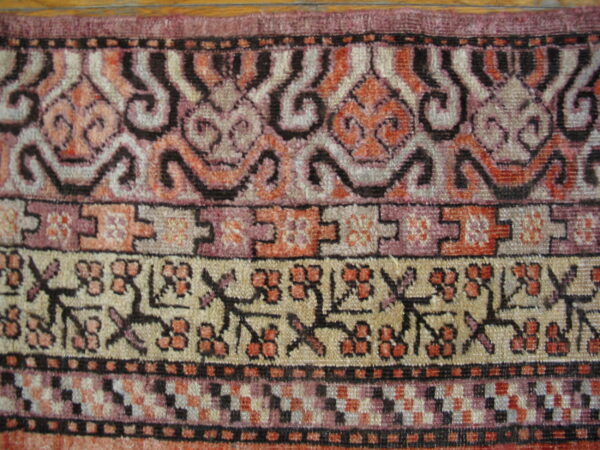 Detailed rug borders show stylized floral, geometric, and scrolling patterns in pink, orange, black, and cream.