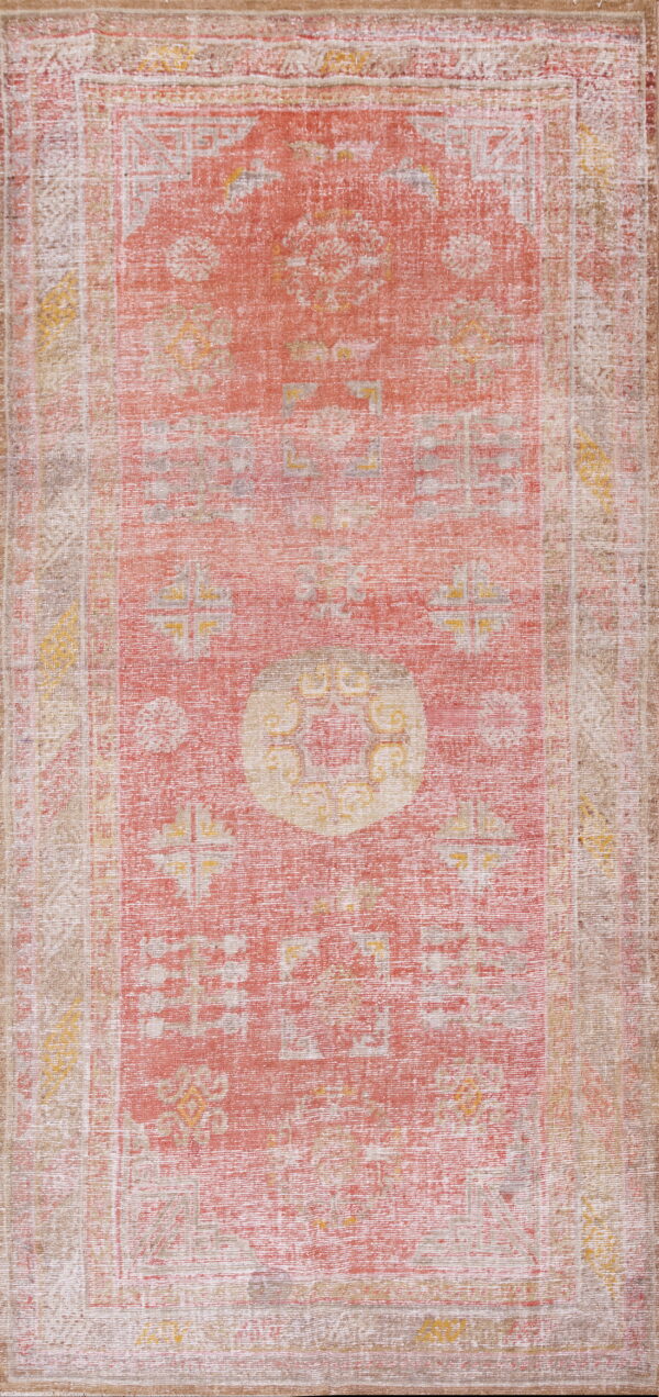 Vertical view of a distressed, low-pile rug featuring faded coral, beige, and yellow geometric patterns.