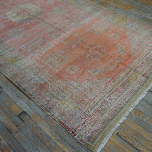 Low-pile, distressed orange, yellow, and beige patterned rug lying on gray and brown wood plank flooring.