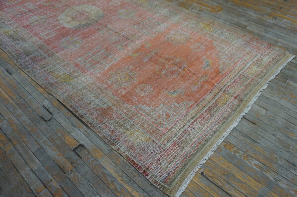 Low-pile, distressed orange, yellow, and beige patterned rug lying on gray and brown wood plank flooring.