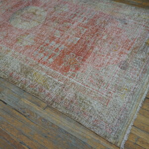 Low-pile distressed rug featuring faded red, white, and khaki patterns lies on worn wood flooring.