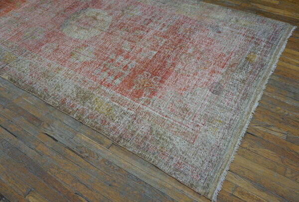 Low-pile distressed rug featuring faded red, white, and khaki patterns lies on worn wood flooring.