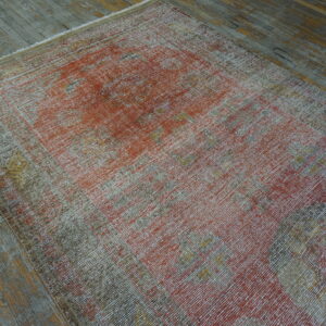 A highly distressed low-pile rug in muted red, gray, and gold lies on worn wooden plank flooring.
