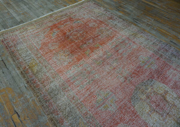 A highly distressed low-pile rug in muted red, gray, and gold lies on worn wooden plank flooring.