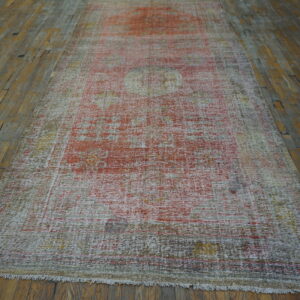 Low-pile runner rug with faded red and cream pattern centered on wide, distressed wood planks.