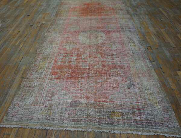 Low-pile runner rug with faded red and cream pattern centered on wide, distressed wood planks.