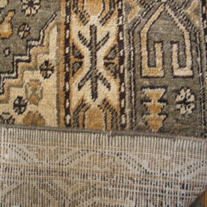 A geometric brown and tan rug is folded back, exposing its woven reverse side on wood flooring.