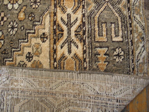 A geometric brown and tan rug is folded back, exposing its woven reverse side on wood flooring.