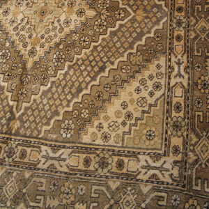 Monochromatic brown rug detail with stepped diamond field patterns and intricate geometric borders on wood planks.