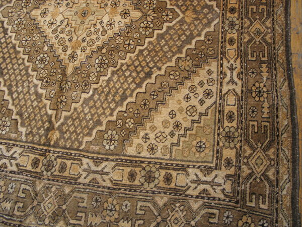 Monochromatic brown rug detail with stepped diamond field patterns and intricate geometric borders on wood planks.