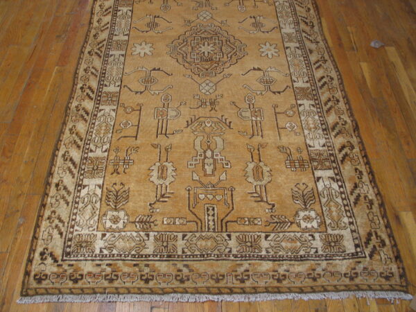 Tan rug with stylized tribal patterns and a central medallion rests on light hardwood planks.