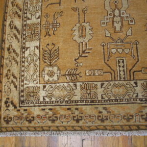 Close-up of a golden brown rug with geometric tribal patterns and fringed edges on wood flooring.