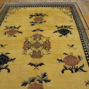 Golden yellow rug with complex brown and navy floral motifs and a geometric border on wood planks.