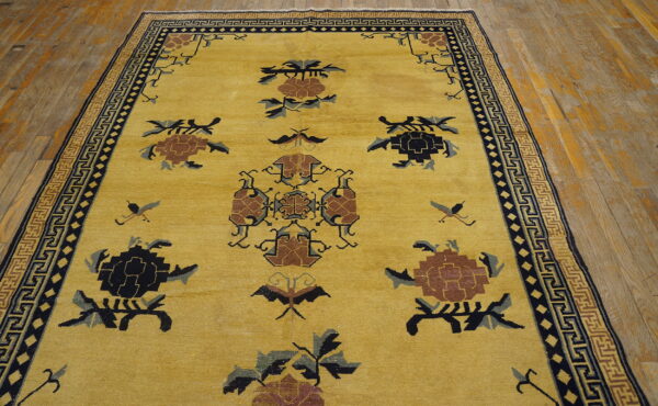 Golden yellow rug with complex brown and navy floral motifs and a geometric border on wood planks.