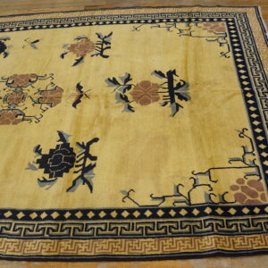 Ornate yellow rug featuring navy and brown patterns and complex geometric fret borders on wood flooring.