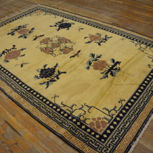 Yellow low-pile rug with scattered floral and insect patterns, bordered by navy meander designs on wood planks.