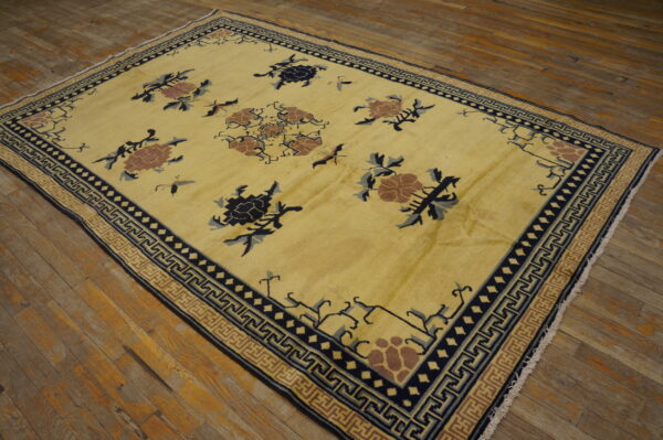 Yellow low-pile rug with scattered floral and insect patterns, bordered by navy meander designs on wood planks.