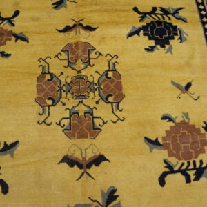 Close-up of a mustard yellow rug featuring geometric motifs in black, brown, and gray, with a detailed key border.