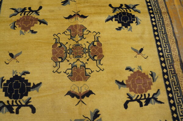 Close-up of a mustard yellow rug featuring geometric motifs in black, brown, and gray, with a detailed key border.