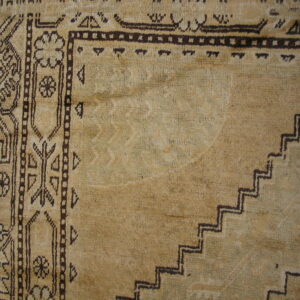 Textured beige rug close-up with dark geometric designs, including stepped patterns and stylized floral motifs.
