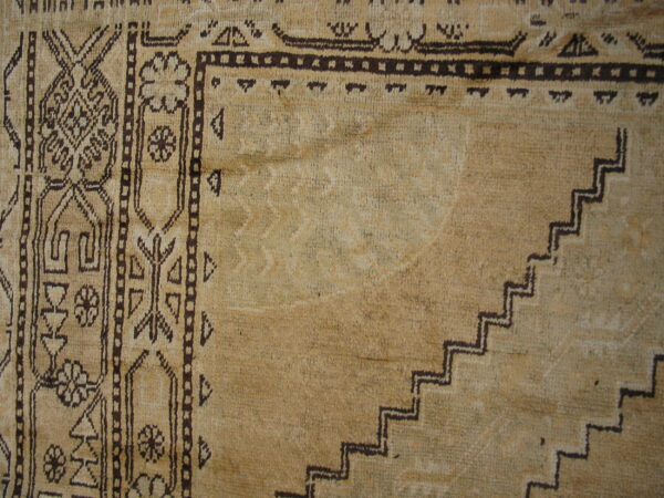 Textured beige rug close-up with dark geometric designs, including stepped patterns and stylized floral motifs.