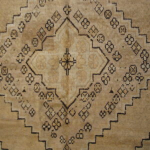 Tan rug detail showing a stepped geometric medallion surrounded by small dark tribal patterns.