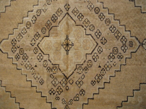 Tan rug detail showing a stepped geometric medallion surrounded by small dark tribal patterns.