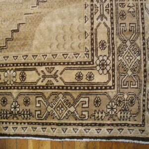 Beige rug corner featuring dark brown geometric and floral borders on hardwood flooring.
