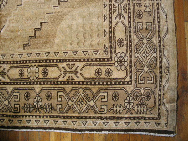 Beige rug corner featuring dark brown geometric and floral borders on hardwood flooring.