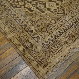 Distressed tan and brown patterned rug corner rests on rustic wood plank flooring.