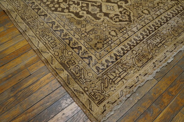 Distressed tan and brown patterned rug corner rests on rustic wood plank flooring.