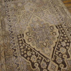 Distressed tan and dark brown traditional rug featuring a geometric medallion rests on rustic plank hardwood floors.