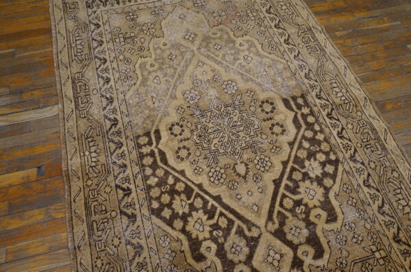 Distressed tan and dark brown traditional rug featuring a geometric medallion rests on rustic plank hardwood floors.