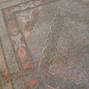 Low-pile rug in muted gray and coral with geometric borders rests on a warm wood plank floor.