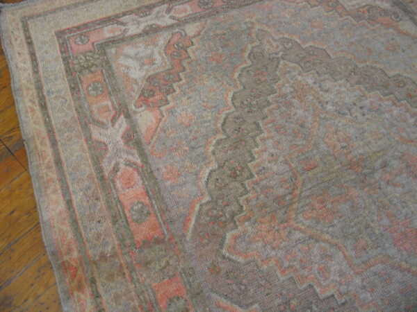 Low-pile rug in muted gray and coral with geometric borders rests on a warm wood plank floor.