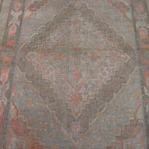 Geometric patterned low-pile rug runner in muted coral and grey lying on a polished hardwood floor.