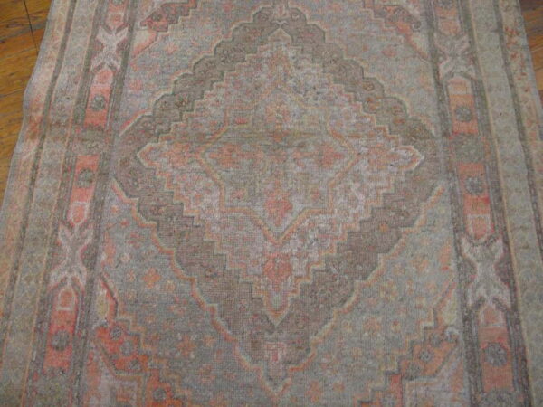 Geometric patterned low-pile rug runner in muted coral and grey lying on a polished hardwood floor.