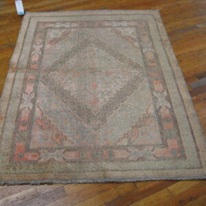 Faded traditional rug featuring gray and salmon geometric patterns rests on a distressed wood plank floor.