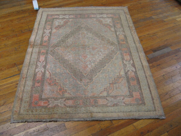 Faded traditional rug featuring gray and salmon geometric patterns rests on a distressed wood plank floor.