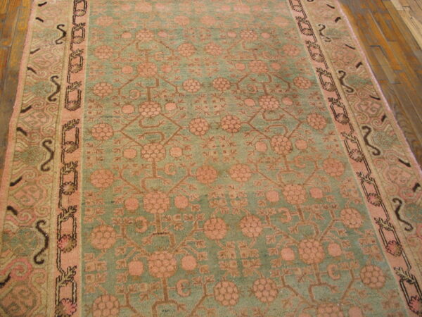 Distressed teal and blush rug with a geometric floral design shown on wide plank hardwood flooring.