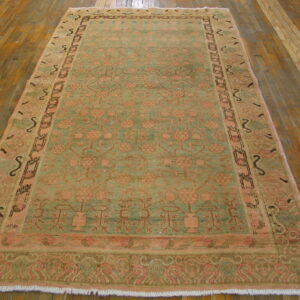 Faded green and coral traditional area rug with botanical patterns lies on wide plank wood floorboards.