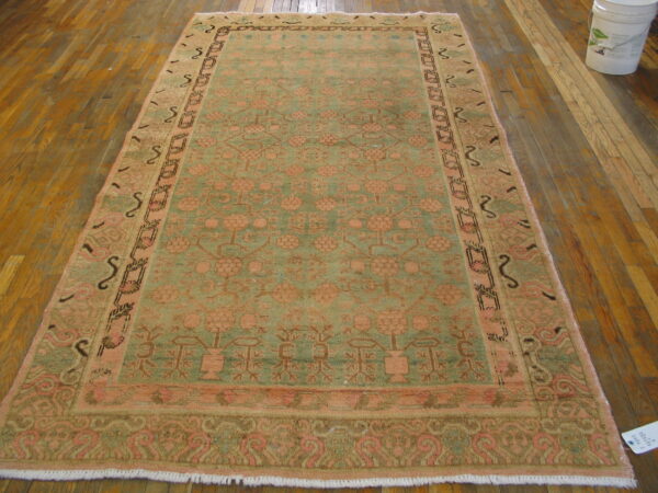 Faded green and coral traditional area rug with botanical patterns lies on wide plank wood floorboards.