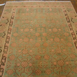 A muted sage and pink traditional rug with repeating floral medallions rests on a dark wood floor.