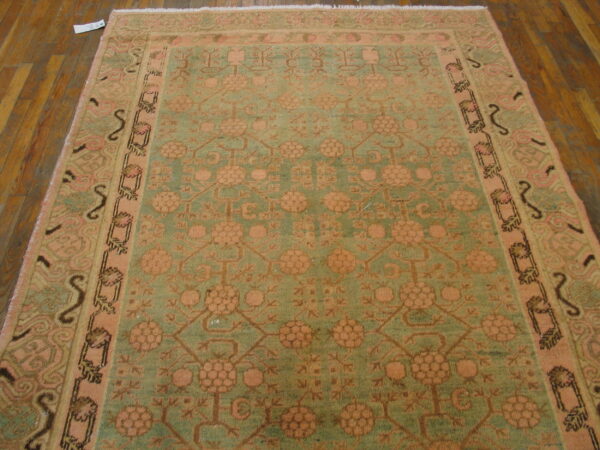 A muted sage and pink traditional rug with repeating floral medallions rests on a dark wood floor.