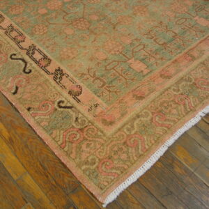 Peach and sage traditional rug with detailed patterns and white fringe rests on distressed hardwood flooring.