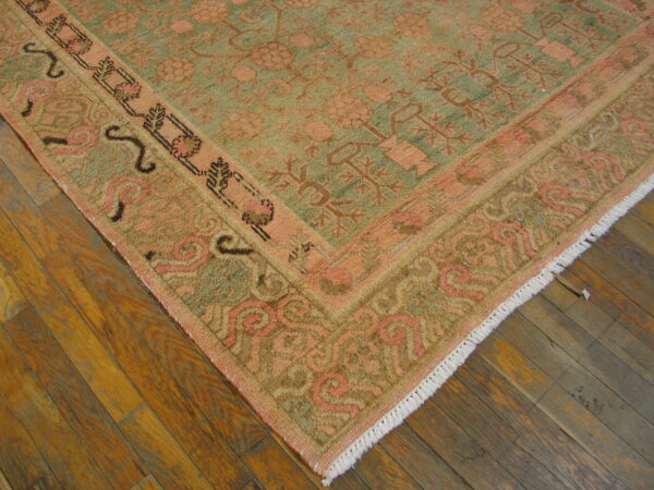 Peach and sage traditional rug with detailed patterns and white fringe rests on distressed hardwood flooring.