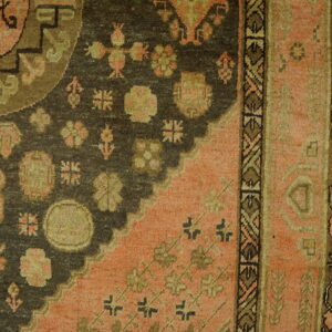 Close-up of a traditional rug with a dark field, pink corner, and geometric motifs on wooden floor.