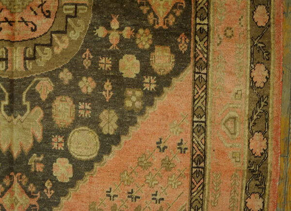 Close-up of a traditional rug with a dark field, pink corner, and geometric motifs on wooden floor.
