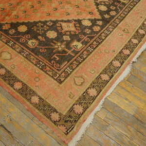 Close-up of a rug corner with coral, tan, and dark brown traditional patterns on distressed wooden floors.